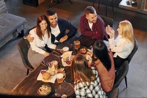 aan het eten en drinken. groep van jong vrienden zittend samen in bar met bier foto