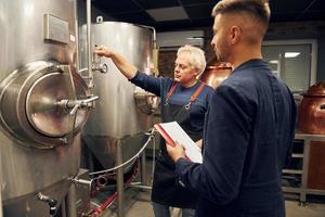 senior Mens en jong arbeider met document is staand in de opslagruimte bier kamer foto