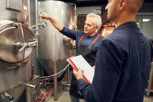 senior Mens en jong arbeider met document is staand in de opslagruimte bier kamer foto