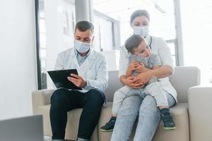 met weinig jongen dat wezen onderzocht. twee artsen in wit jassen is in de kliniek werken samen foto