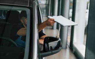 zittend in voertuig en Holding document. levering Mens in uniform is binnenshuis met auto en met bestellen foto