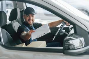 vrolijk arbeider. levering Mens in uniform is binnenshuis met auto en met bestellen foto