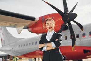 Bij dag. jong stewardess dat is in formeel zwart kleren is staand buitenshuis in de buurt vlak foto