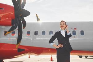 op zoek ver weg. jong stewardess dat is in formeel zwart kleren is staand buitenshuis in de buurt vlak foto