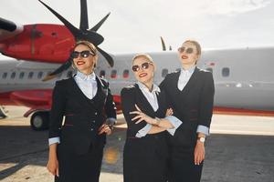 drie mensen. bemanning van luchthaven en vlak arbeiders in formeel kleren staand buitenshuis samen foto