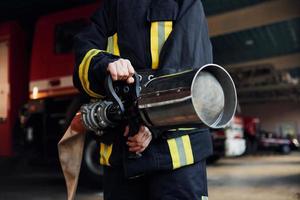 slang in handen. vrouw brandweerman in beschermend uniform staand in de buurt vrachtauto foto