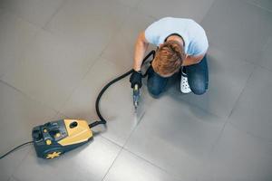 top visie van Mens in blauw overhemd en beschermend handschoenen dat toepassingen vacuüm schoonmaakster foto