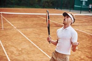 vieren zege. jong tennis speler in sportief kleren is Aan de rechtbank buitenshuis foto