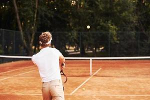 jong tennis speler in sportief kleren is Aan de rechtbank buitenshuis foto