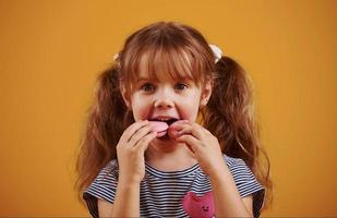 schattig weinig meisje met zoet voedsel in de studio tegen geel achtergrond foto