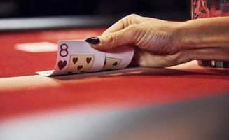 dichtbij omhoog visie van vrouw handen. meisje Toneelstukken poker spel door tafel in casino en cheques kaarten foto