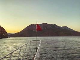 jacht in de Open zee. zee met een zanderig strand tegen de backdrop van een berg. de Turks rood vlag is geïnstalleerd Aan de streng van de jacht foto