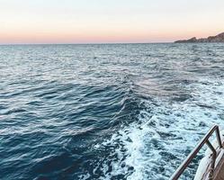 wandelen Aan de Open zee. blauw golven van de zee Aan de achtergrond van de zonsondergang. de jacht is uitgerust met metaal zijden voor de veiligheid van toeristen. vakantie in heet landen foto