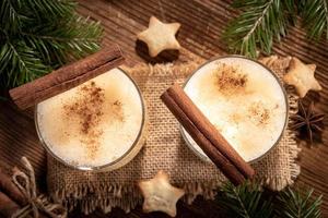 traditioneel Kerstmis Advocaat met kaneel in twee bril, Spar takken, koekjes sterren Aan houten tafel. foto