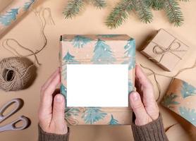 vrouw handen Holding Kerstmis geschenk doos verpakt in feestelijk papier met kopiëren ruimte Aan beige. top visie. foto