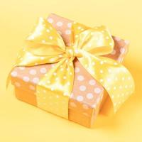 geschenk doos verpakt door polka punt ambacht papier met geel polka punt boog Aan geel dichtbij omhoog. foto