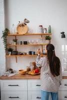 vrouw duurt uit een glas van plank in de keuken foto