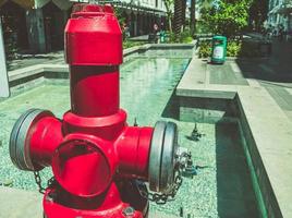 helder, rood brand hydrant. water naar blussen branden Aan de straat. een groot metaal brand hydrant De volgende naar een water fontein. veiligheid van mensen Aan de straat van rook en brand foto