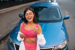 vrouw gebruik makend van mobiel telefoon in de buurt auto Bij de straat foto