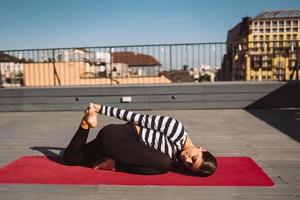 vrouw aan het doen yoga opdrachten Aan huis dak in vroeg ochtend- foto