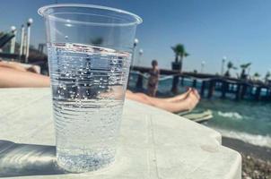 een plastic glas is Aan de tafel, een transparant koolzuurhoudend drinken is gegoten binnen. ontspannende Aan de strand, koeling de lichaam met drankjes. lichaam water foto