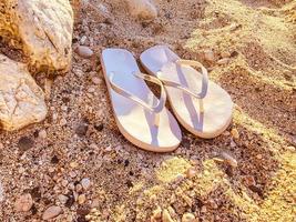 wit rubber slippers staan Aan de zand. zee schoenen. leien voor wandelen langs de zee kust. vrouwen slippers dat zijn versleten Aan een vinger foto
