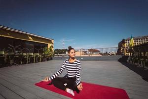 jong vrouw mediteren in lotus houding Bij dak van de gebouw foto