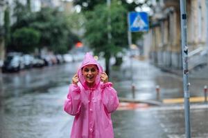 jong glimlachen vrouw met regenjas terwijl genieten van een regenachtig dag. foto