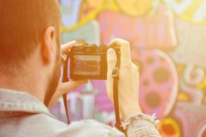 een jong graffiti artiest foto's zijn voltooid afbeelding Aan de muur. de vent toepassingen modern technologie naar vastleggen een kleurrijk abstract graffiti tekening. focus Aan de fotograferen apparaat foto