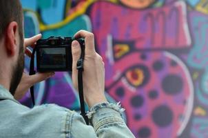 een jong graffiti artiest foto's zijn voltooid afbeelding Aan de muur. de vent toepassingen modern technologie naar vastleggen een kleurrijk abstract graffiti tekening. focus Aan de fotograferen apparaat foto