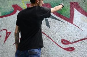 een jong hooligan verven graffiti Aan een beton muur. onwettig vandalisme concept. straat kunst foto