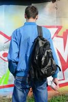 een jong graffiti artiest met een zwart zak looks Bij de muur met zijn graffiti Aan een muur. straat kunst concept foto