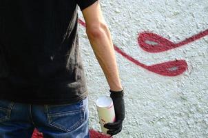 een jong hooligan met een verstuiven kan staat tegen een beton muur met graffiti schilderijen. onwettig vandalisme concept. straat kunst foto