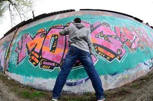 een jong vent in een grijs capuchon verven graffiti in roze en groen c foto