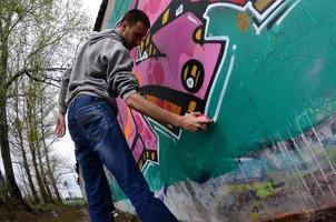 een jong vent in een grijs capuchon verven graffiti in roze en groen c foto