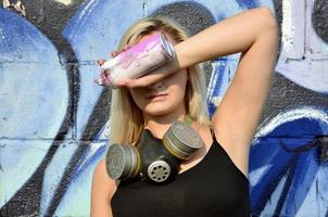 jong en mooi sexy meisje graffiti artiest met gas- masker Aan haar nek schuilplaats zijn ogen met een verstuiven kan staand Aan een muur achtergrond met een graffiti patroon in blauw en Purper tonen foto