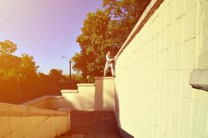 een jong vent overwint obstakels, beklimming Aan beton muren. de atleet praktijken parkour, opleiding in straat conditie. de concept van sport- subculturen tussen jeugd foto