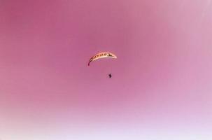 paragliden in een heet land. Parachutespringen van de berg, actief recreatie. een Mens in een beschermend pak is vliegend in een heet lucht ballon Aan een roze schattig lucht foto
