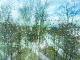 reflectie in glas, venster van een meerdere verdiepingen gebouw. regendruppels Aan de glas. textuur, achtergrond. tegen de backdrop van bomen, planten en groen in de regen foto