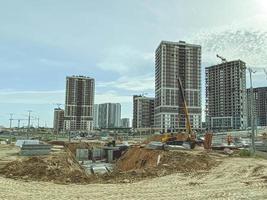 bouw van een nieuw buurt in de stad. erectie van hoog, meerdere verdiepingen gebouwen gemaakt van concreet, glas, blokken. graven een fundament pit dichtbij foto