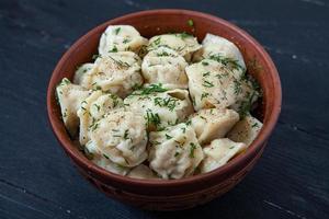 traditioneel Russisch pelmeni of ravioli, knoedels met vlees Aan hout zwart achtergrond. Russisch voedsel en Russisch keuken concept. foto