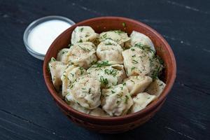 traditioneel Russisch pelmeni of ravioli, knoedels met vlees Aan hout zwart achtergrond. Russisch voedsel en Russisch keuken concept. foto