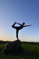 silhouet van jong blond meisje in sport pak praktijk yoga Aan een pittoreske groen heuvel in de avond Bij zonsondergang. de concept van oefenen en gezond levensstijlen foto