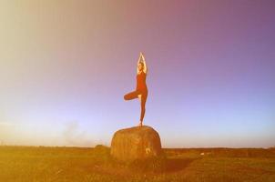 silhouet van jong blond meisje in sport pak praktijk yoga Aan een pittoreske groen heuvel in de avond Bij zonsondergang. de concept van oefenen en gezond levensstijlen foto