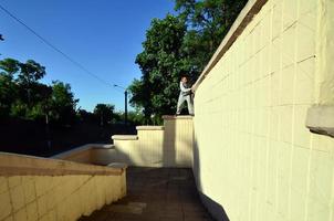 een jong vent overwint obstakels, beklimming Aan beton muren. de atleet praktijken parkour, opleiding in straat conditie. de concept van sport- subculturen tussen jeugd foto