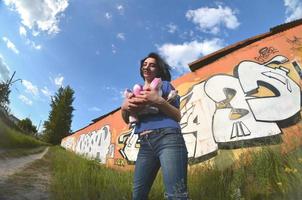 portret van een emotioneel jong meisje met zwart haar- en piercings. een wijde hoek foto van een meisje met aërosol verf blikjes in de handen Aan een graffiti muur achtergrond. een modern portret van een vissenoog lens