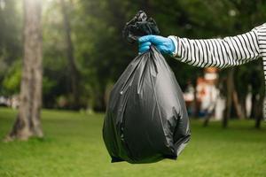 hand- Holding vuilnis zwart zak zetten in naar uitschot naar schoon. opruimen, vervuiling, en plastic concept. foto