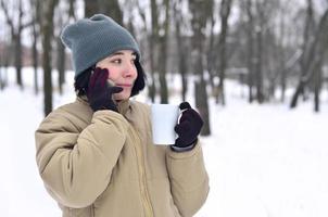 winter portret van jong meisje met smartphone en koffie kop foto