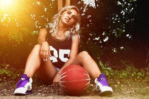 jong blond meisje met oranje basketbal poseren buitenshuis foto