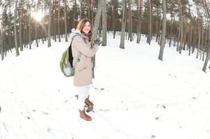 een jong en blij Kaukasisch meisje in een bruin jas houdt een sneeuwbal in een met sneeuw bedekt Woud in winter. vissenoog foto